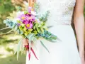 Piękny bukiet ślubny z margaretkami i zielenią, trzymany przez pannę młodą w białej sukni.