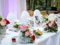 Kwiaty na stół pary młodej jak zrobić? Eleganckie bukiety róż i goździków zdobią biały obrus.