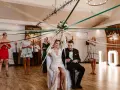 Panna młoda z welonem z wstążek, siedząca obok pana młodego. Wokół tańczące kobiety, tworzące tradycyjne oczepiny inaczej.
