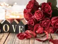 Bukiet czerwonych róż, świeca i napisy "LOVE" na drewnianym stole. Idealna dekoracja na 11 rocznicę ślubu, znaną jako rocznica stalowa.