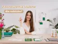 Uśmiechnięta kobieta przy biurku z zaproszeniami ślubnymi. Czy rodzicom daje się zaproszenie na ślub? Na stole leżą próbki zaproszeń i kwiaty.