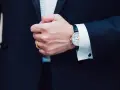 Mężczyzna w garniturze zapina mankiet koszuli, pokazując zegarek i spinki do mankietów. Jak założyć spinki do mankietów?