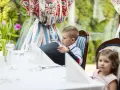 Chłopiec przy weselnym stole dla dzieci przegląda menu. Obok siedzi dziewczynka.