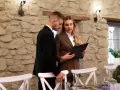 Para weselnych planuje, jak usadzić gości na weselu, przeglądając listę przy kamiennej ścianie.