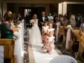 Panna młoda z bukietem idzie do ołtarza w kościele ślubnym, a za nią podążają dziewczynki sypiące kwiaty.
