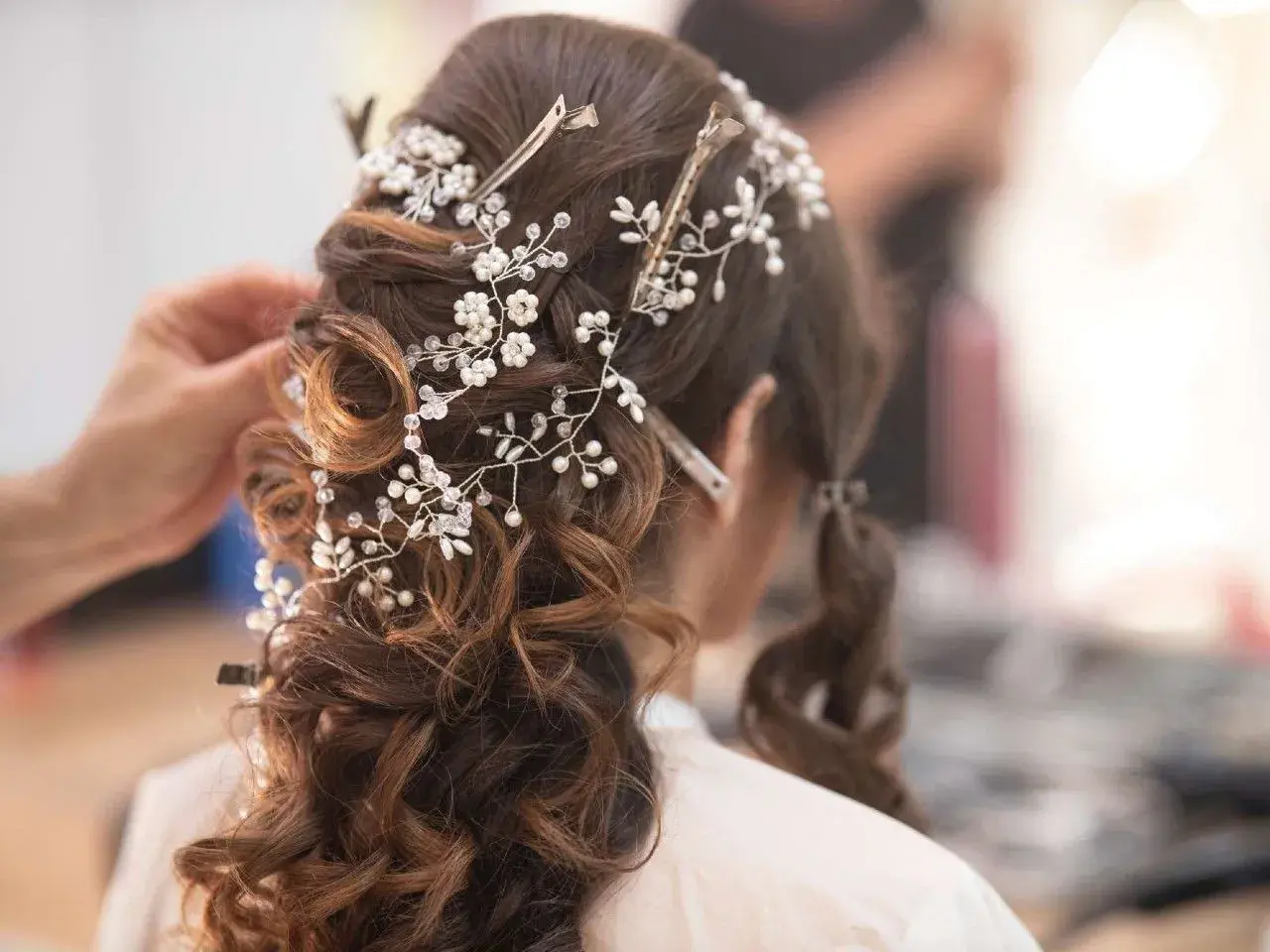 Eleganckie fryzury ślubne z perłami i kryształkami, tworzące romantyczny wianek na brązowych włosach.