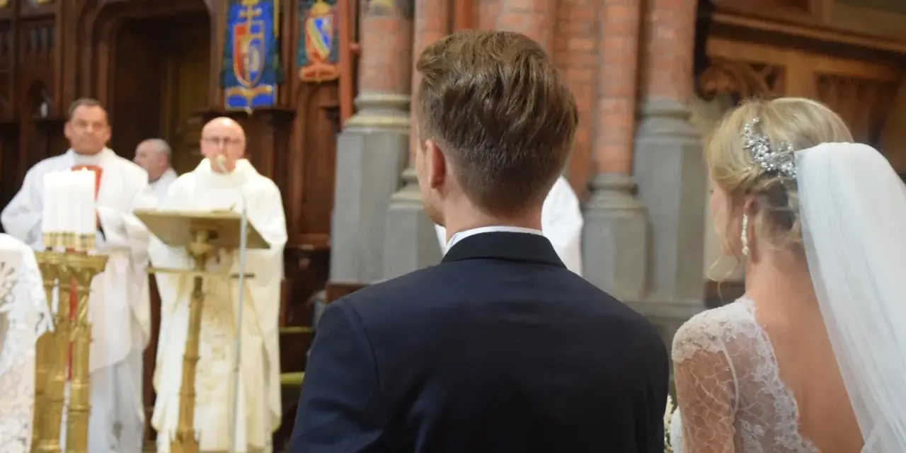 W kościele podczas ślubu, ksiądz czyta wiersze o miłości. Panna młoda w welonie i pan młody w garniturze słuchają.