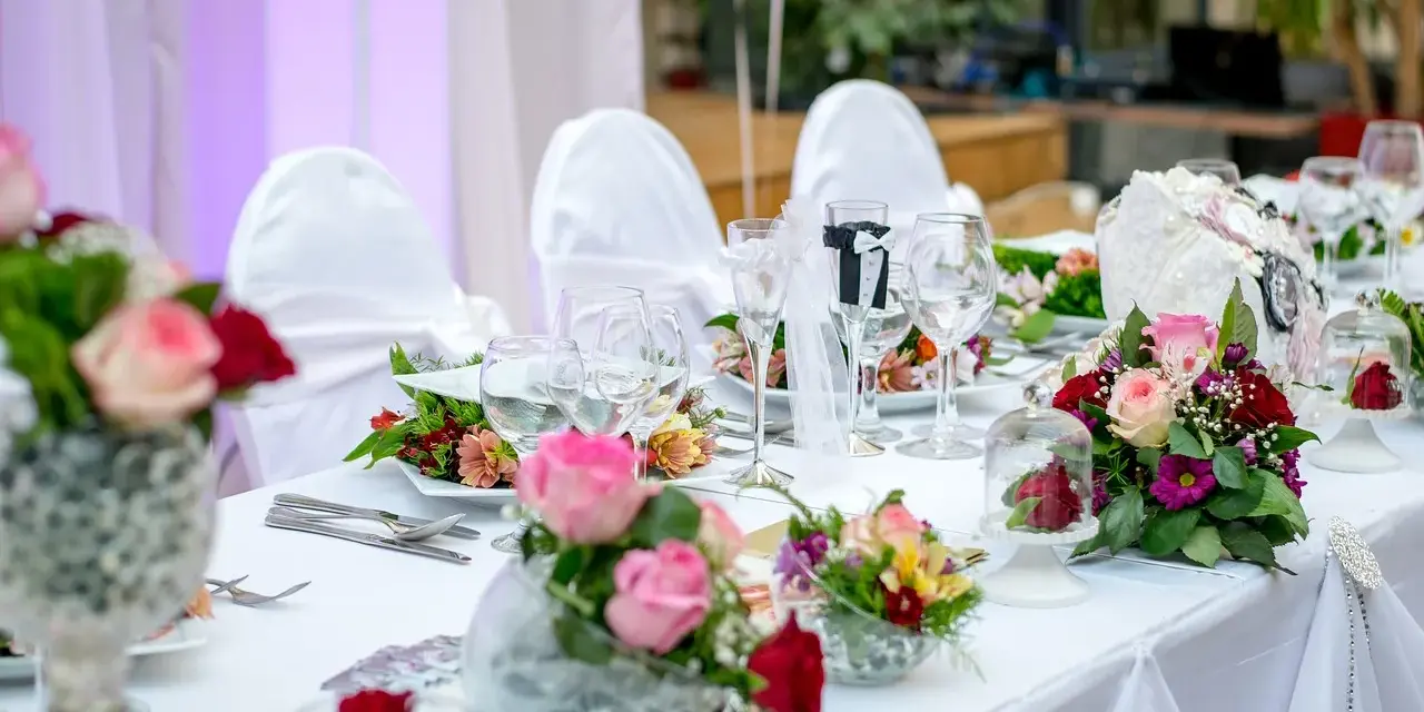 Kwiaty na stół pary młodej jak zrobić? Eleganckie bukiety róż i goździków zdobią biały obrus.