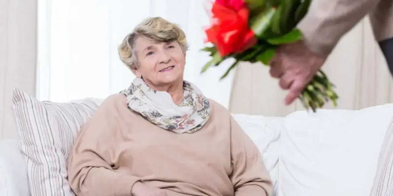 Uśmiechnięta starsza pani otrzymuje bukiet czerwonych róż. To piękny gest z okazji 75 rocznicy ślubu.