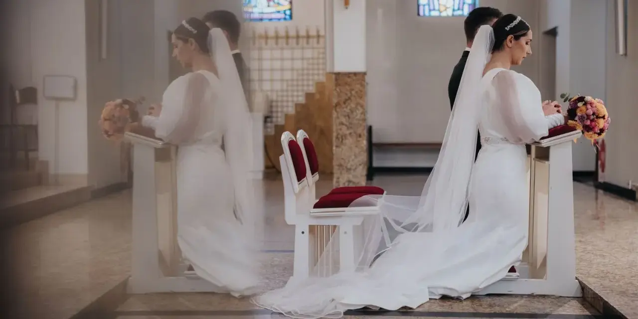 Panna młoda klęczy przy ołtarzu, obok niej stoi pan młody. W kościele widać witraże i ławki. Czyżby żonaty świadek na ślubie przesądy?