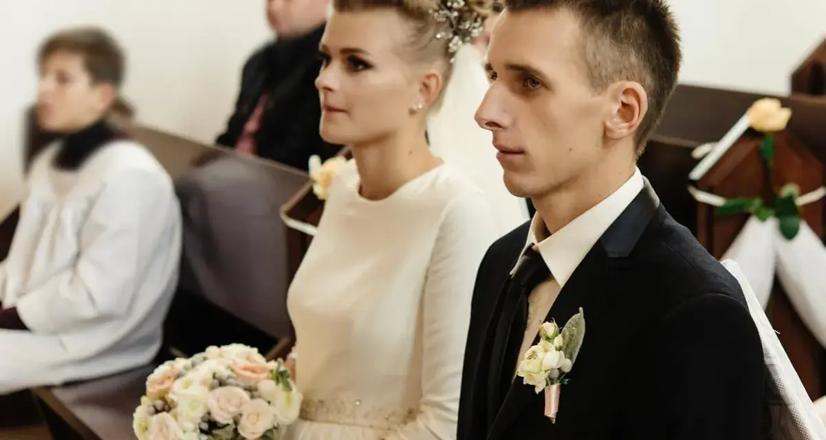 Para młoda w kościele, ona z bukietem, on w garniturze. Ceremonia ślubna, choć w żałobie, odbywa się z godnością.