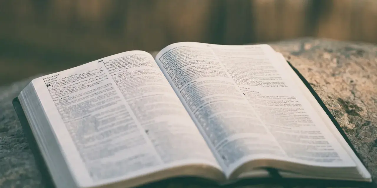 Otwarta Biblia na kamieniu, strony z tekstem, widoczny psalm 33:1. Może to być psalm ślubny.