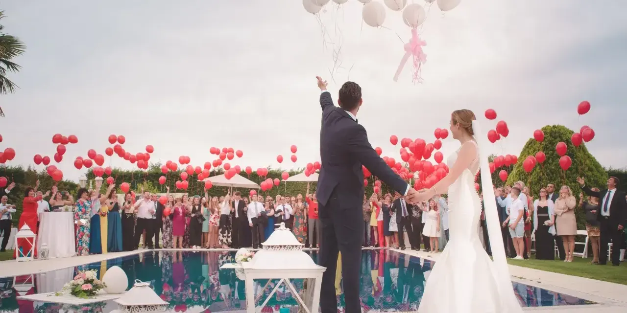 Para młoda wypuszcza balony podczas wesela w piątek. Goście trzymają czerwone balony, a para młoda białe.