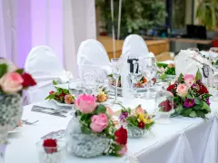 Kwiaty na stół pary młodej jak zrobić? Eleganckie bukiety róż i goździków zdobią biały obrus.