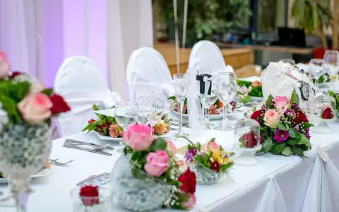 Kwiaty na stół pary młodej jak zrobić? Eleganckie bukiety róż i goździków zdobią biały obrus.