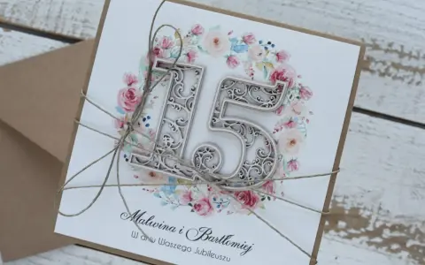 Elegancka kartka z napisem "Malwina i Bartłomiej w dniu Waszego Jubileuszu" i ozdobnym numerem "15" na tle kwiatów. To zaproszenie na 15 rocznicę ślubu, zwaną rocznicą szklaną.