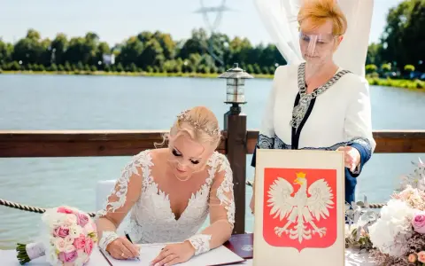 Panna młoda w sukni ślubnej podpisuje dokumenty, obok urzędniczka z herbem Polski. Jej stan cywilny rozwodnik nie przeszkodził w tym radosnym dniu.