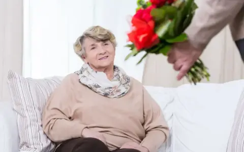 Uśmiechnięta starsza pani otrzymuje bukiet czerwonych róż. To piękny gest z okazji 75 rocznicy ślubu.