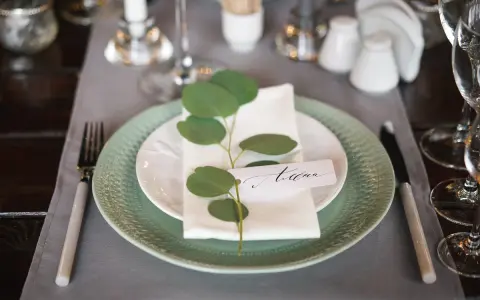 Eleganckie winietki co to? Pięknie nakryty stół z zieloną gałązką i imieniem gościa.