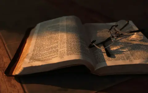 Otwarta Biblia z okularami, oświetlona ciepłym światłem. Co znaczy vel przed nazwiskiem? To skrót od "vel" (łac. "albo"), używany w dokumentach, by wskazać alternatywne nazwisko.