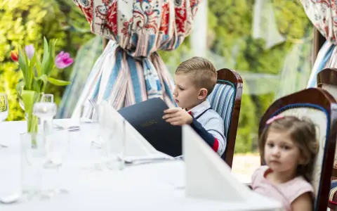 Chłopiec przy weselnym stole dla dzieci przegląda menu. Obok siedzi dziewczynka.