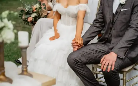 Para szybko wziąć ślub kościelny, para młoda trzyma się za ręce. Panna młoda w sukni z koronki, pan młody w garniturze.
