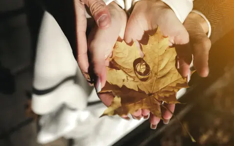 Dłonie trzymają jesienny liść z obrączkami. To symbol 22 rocznicy ślubu, która przypada na jesień.