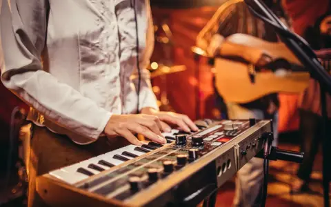 Muzyk gra na keyboardzie, tworząc tło dla najpiękniejszych piosenek biesiadnych. W tle widać gitarzystę.