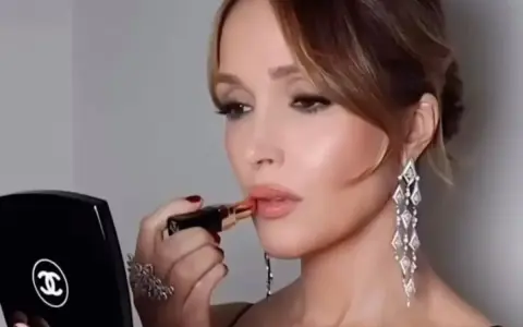 Elegancka kobieta z makijażem weselnym nakłada szminkę, patrząc w lusterko Chanel.