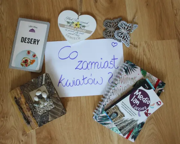 Co zamiast kwiatów na wesele? Na stole leżą karty z deserami, książki o podróżach i serce z napisem "Niech Twój uśmiech zmienia świat".
