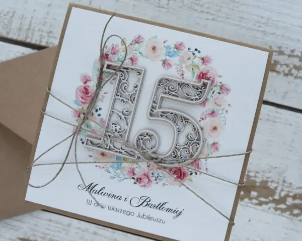 Elegancka kartka z napisem "Malwina i Bartłomiej w dniu Waszego Jubileuszu" i ozdobnym numerem "15" na tle kwiatów. To zaproszenie na 15 rocznicę ślubu, zwaną rocznicą szklaną.