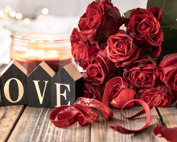 Bukiet czerwonych róż, świeca i napisy "LOVE" na drewnianym stole. Idealna dekoracja na 11 rocznicę ślubu, znaną jako rocznica stalowa.