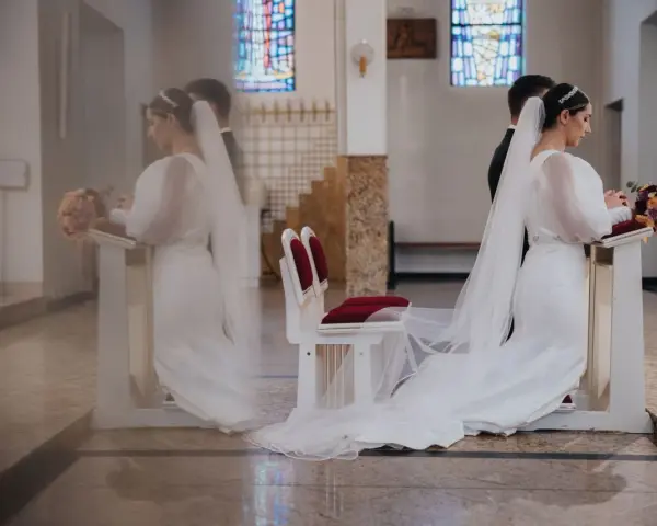 Panna młoda klęczy przy ołtarzu, obok niej stoi pan młody. W kościele widać witraże i ławki. Czyżby żonaty świadek na ślubie przesądy?