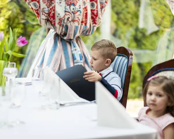 Chłopiec przy weselnym stole dla dzieci przegląda menu. Obok siedzi dziewczynka.