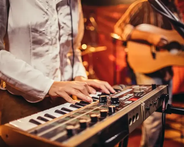 Muzyk gra na keyboardzie, tworząc tło dla najpiękniejszych piosenek biesiadnych. W tle widać gitarzystę.
