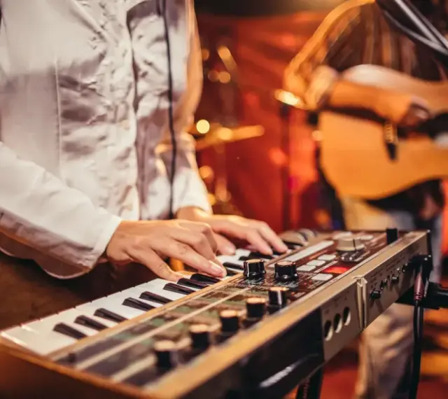 Muzyk gra na keyboardzie, tworząc tło dla najpiękniejszych piosenek biesiadnych. W tle widać gitarzystę.