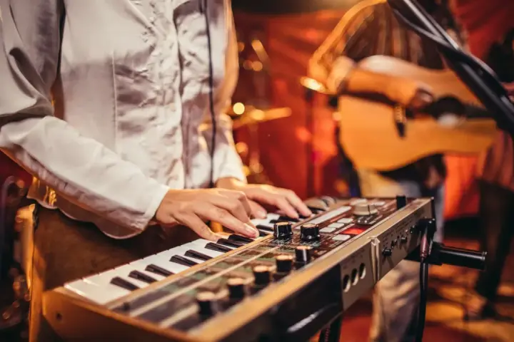 Muzyk gra na keyboardzie, tworząc tło dla najpiękniejszych piosenek biesiadnych. W tle widać gitarzystę.