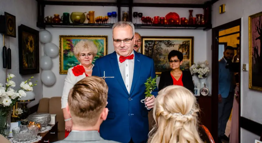 Uroczysty błogosławieństwo przed ślubem cywilnym. Mężczyzna w garniturze trzyma krzyżyk i gałązkę.
