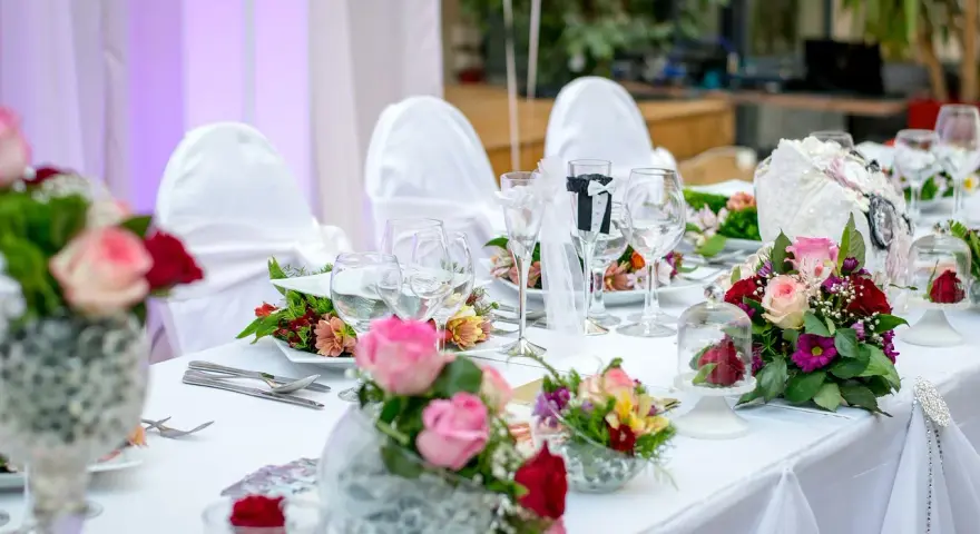 Kwiaty na stół pary młodej jak zrobić? Eleganckie bukiety róż i goździków zdobią biały obrus.