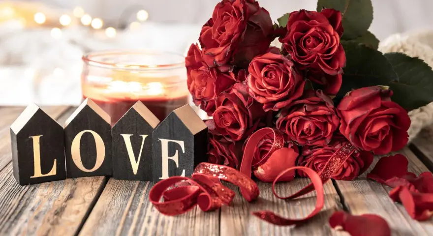 Bukiet czerwonych róż, świeca i napisy "LOVE" na drewnianym stole. Idealna dekoracja na 11 rocznicę ślubu, znaną jako rocznica stalowa.