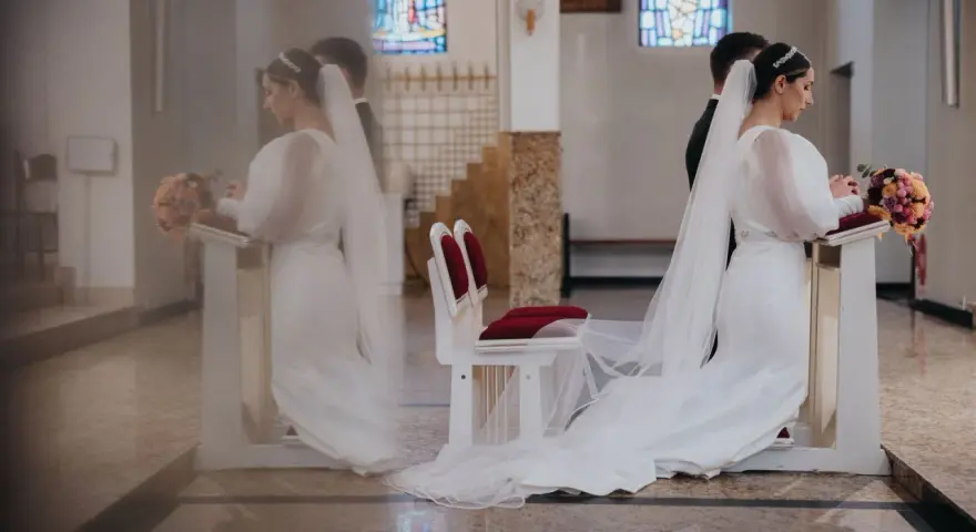 Panna młoda klęczy przy ołtarzu, obok niej stoi pan młody. W kościele widać witraże i ławki. Czyżby żonaty świadek na ślubie przesądy?