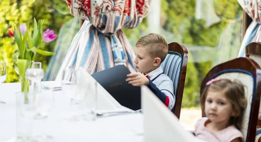 Chłopiec przy weselnym stole dla dzieci przegląda menu. Obok siedzi dziewczynka.