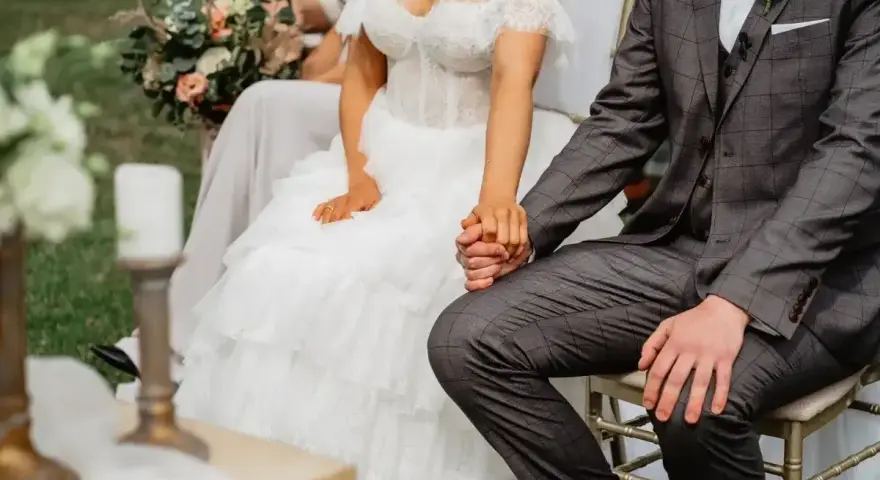Para szybko wziąć ślub kościelny, para młoda trzyma się za ręce. Panna młoda w sukni z koronki, pan młody w garniturze.
