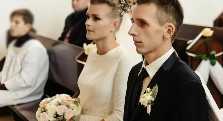 Para młoda w kościele, ona z bukietem, on w garniturze. Ceremonia ślubna, choć w żałobie, odbywa się z godnością.