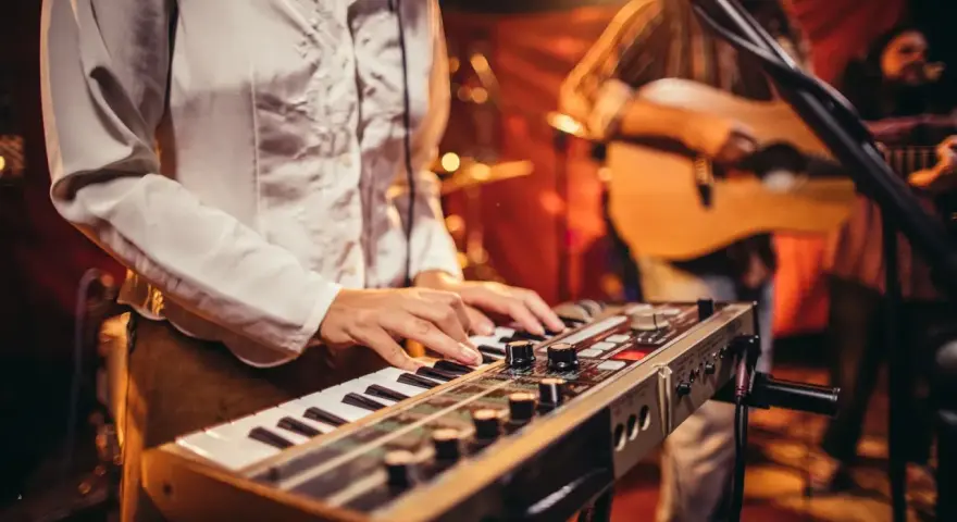 Muzyk gra na keyboardzie, tworząc tło dla najpiękniejszych piosenek biesiadnych. W tle widać gitarzystę.