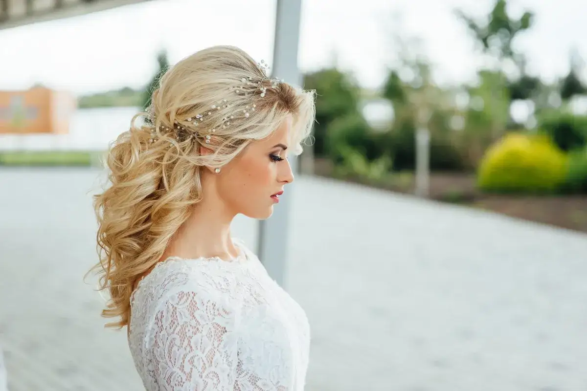 Blondynka w białej sukni z lokami i ozdobami we włosach, profil.