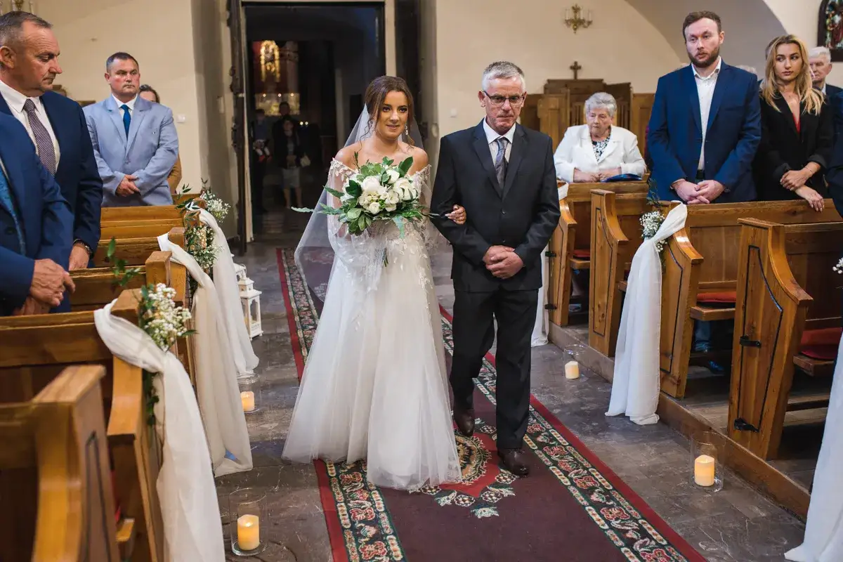Panna młoda z bukietem idzie do ołtarza z ojcem. Ślub kościelny to sakrament, który daje błogosławieństwo i jednoczy dwoje ludzi.