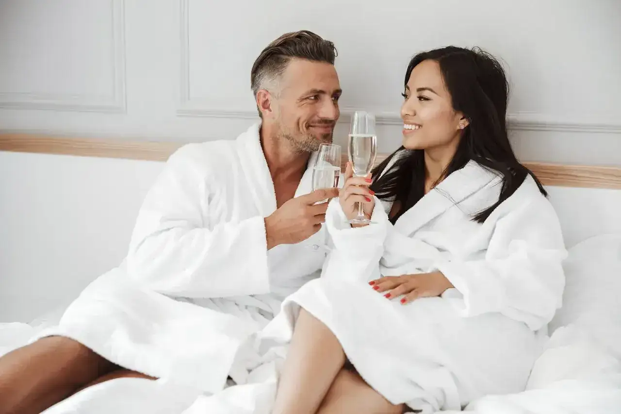 Para świętuje 13 rocznicę ślubu, toast szampanem w białych szlafrokach.