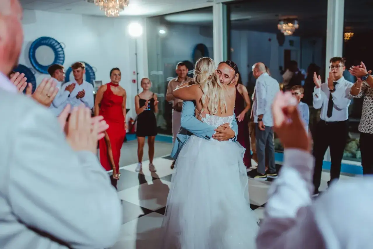 Para dowiedzieć się, o co zapytać fotografa ślubnego, zobacz tę parę podczas pierwszego tańca, otoczoną przez gości klaszczących na weselu.