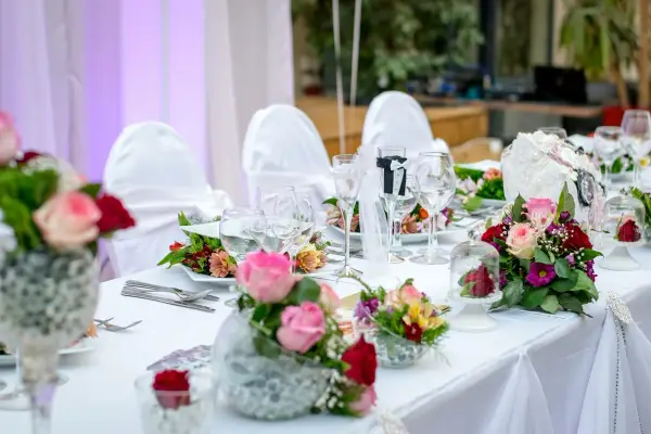 Kwiaty na stół pary młodej jak zrobić? Eleganckie bukiety róż i goździków zdobią biały obrus.